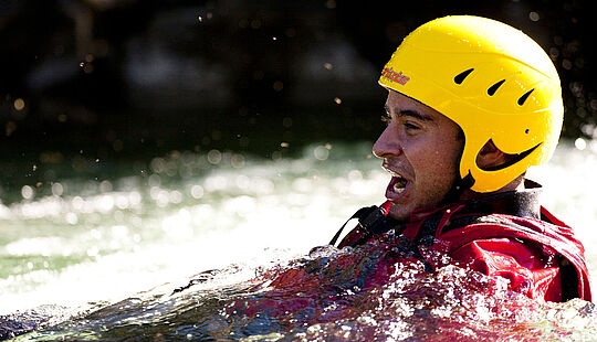 Person mit Helm, Schwimmweste und Neoprenanzug schwimmt im Wasser und genießt die Action