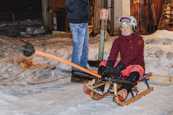 Eine Person sitzt auf einem Schlitten und wird vom Schlepplift den Hang hinaufgezogen