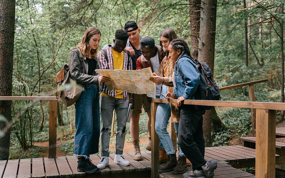 Team im Wald bei einem Teamevent schaut gemeinsam auf eine Karte und sucht den Weg