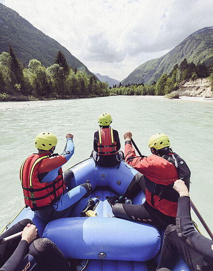 Perspektive aus dem Raftingboot: Personen sitzen im Boot und fahren gemeinsam den Fluss hinunter