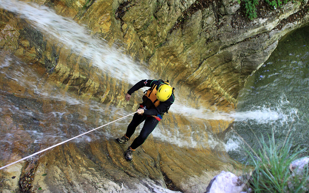 Person wird beim Canyoning in Tirol einen Wasserfall hinab abgeseilt