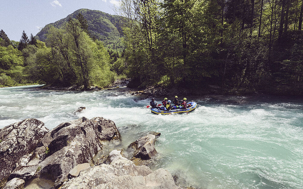 Raftingboot fährt die Isar hinunter durch eine idyllische Landschaft mit Wald und Bergen im Hintergrund