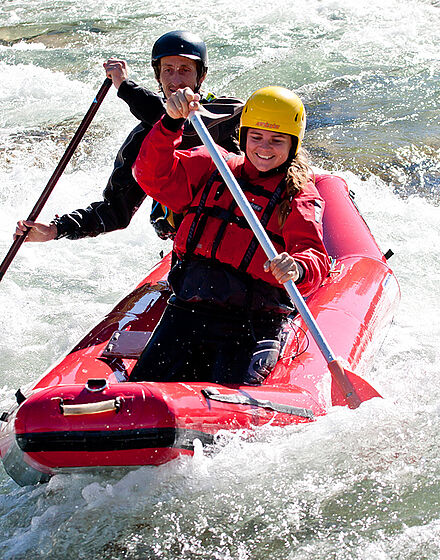 Zwei Personen im Schlauchkanadier paddeln fröhlich bei der Kanutour auf der Isar in Bayern