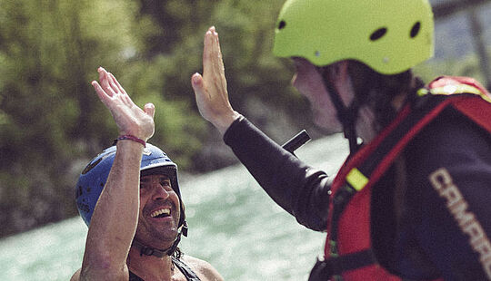 wei lachende Personen geben sich nach der Tour ein High Five, im Hintergrund fließt die Isar
